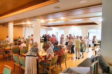 Auf diesem Bild sind viele Gäste zu sehen. Einige sitzen am Tisch, andere Tanzen.