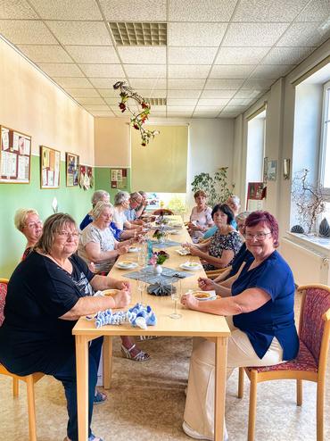 Auf dem Bild sind einige Besucher des Vortrages zu sehen. Alle sitzen gemeinsam am Tisch und lächeln in die Kamera.