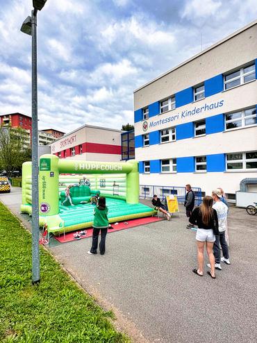Auf diesem Bild ist die KITA von außen zu sehen. Davor steht eine Hüpfburg in Benutzung.