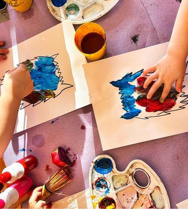 Auf diesem Bild sind die Kinder von oben fortografiert. Sie sitzen an einem Tisch und bearbeiten die Kunstwerke für den Zaun. Es wird gemalt, gebastelt und gepinselt.