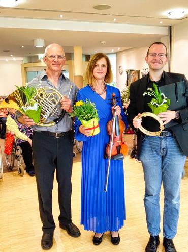Auf dem Bild sind 3 Künstler zu sehen. Sie halten verschiedene Instrumente in der Hand und wirken allgemein fröhlich und nahbar.