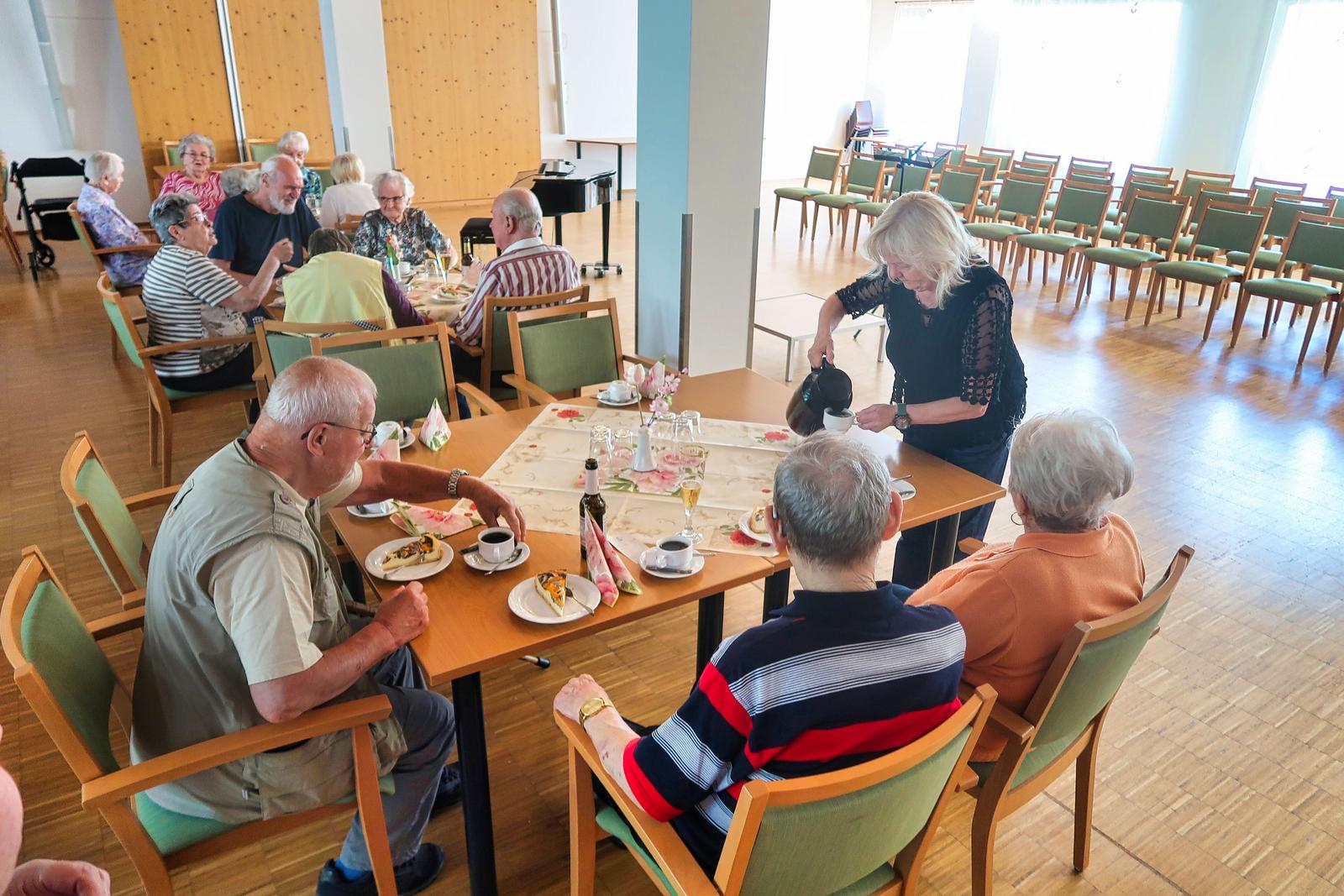 Auf diesem Bild sieht man einige Gäste, an einem Tisch sitzend. Diese werde von einer Mitarbeiterin bedient welche Ihnen Kaffee einschänkt.