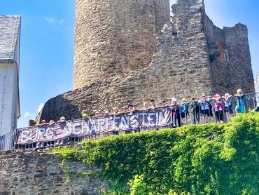 Auf diesem Bild sind die Schulanfänger der KITA Pfiffikus auf der Brüstung der Burg Scharfenstein zu erkennen. Sie halten ein Banner mit der Aufschrift "Burg Scharfenstein" in den Händen.
