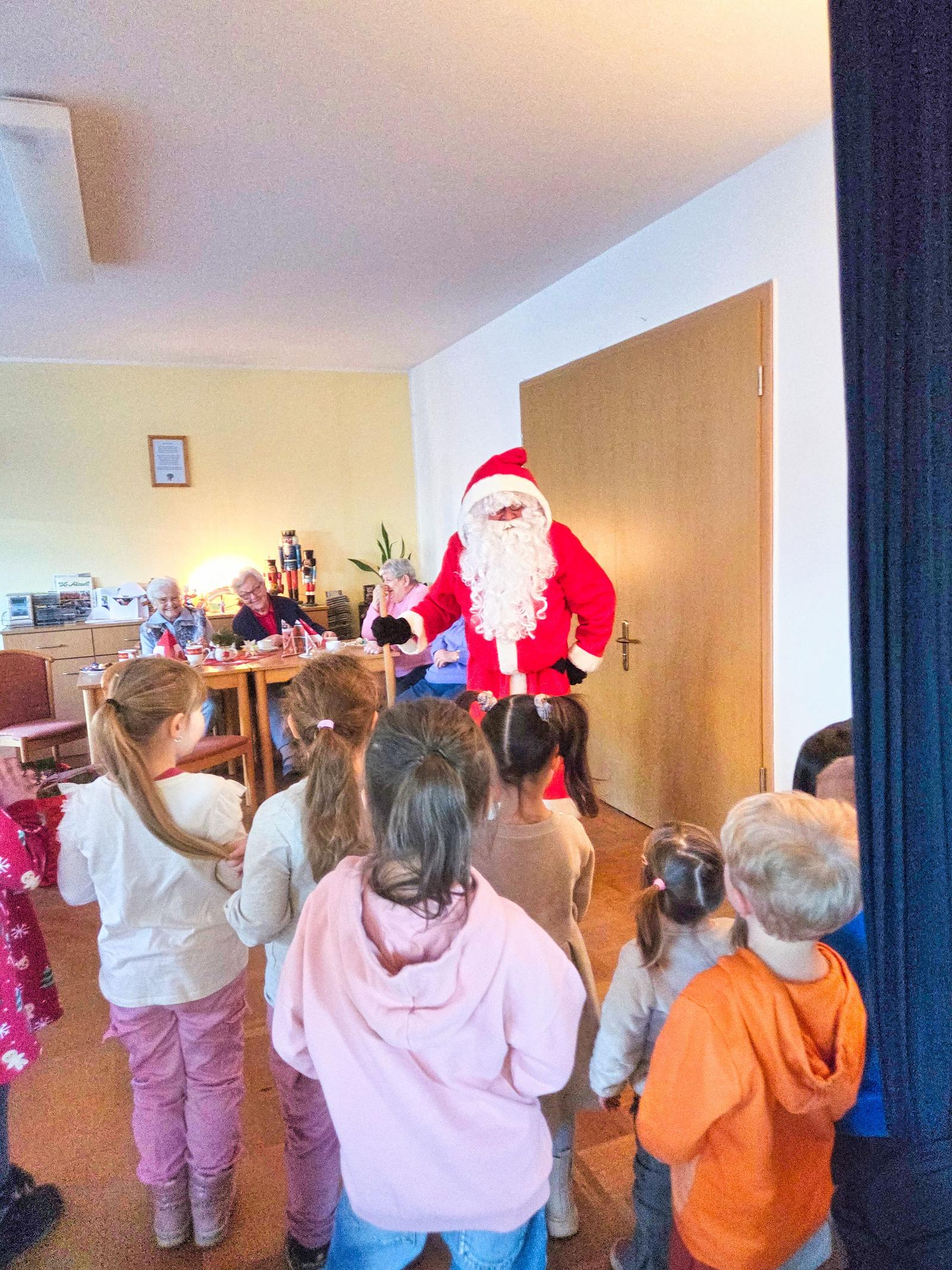 Auf diesem Bild ist der Weihnachtsmann zu sehen. Die Kinder singen Ihm etwas vor und bekommen Geschenke. 