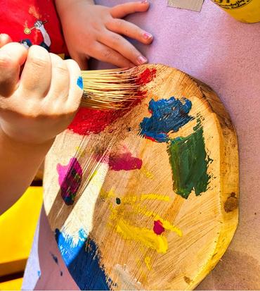 Auf diesem Bild sind die Kinder von oben fortografiert. Sie sitzen an einem Tisch und bearbeiten die Kunstwerke für den Zaun. Es wird gemalt, gebastelt und gepinselt.