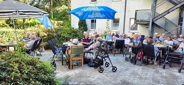 Auf dem Bild sind einige teilnehmer des Festes an den Tischen zu sehen. Die Stimmung ist heiter.